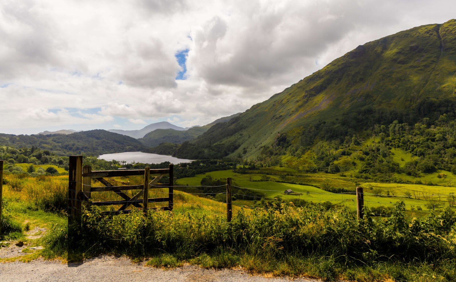 Llyn Gwynant and the Nant Gwynant Valley in Eryri, North Wales, surrounded by dramatic green mountains beneath a cloudy summer sky.