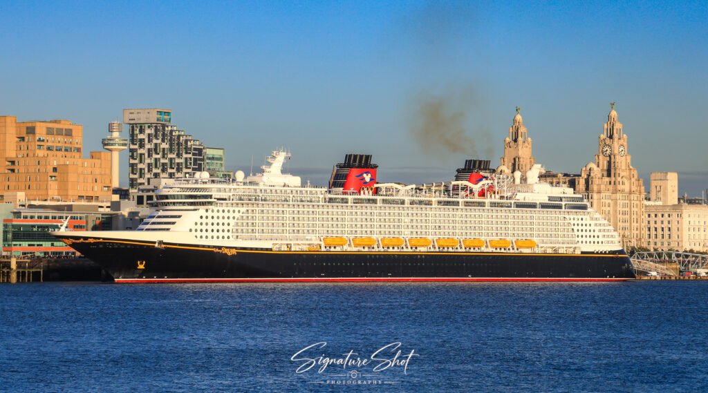 Disney Dream cruise ship docked on the River Mersey with Liverpool’s Royal Liver Building and waterfront skyline in the background.