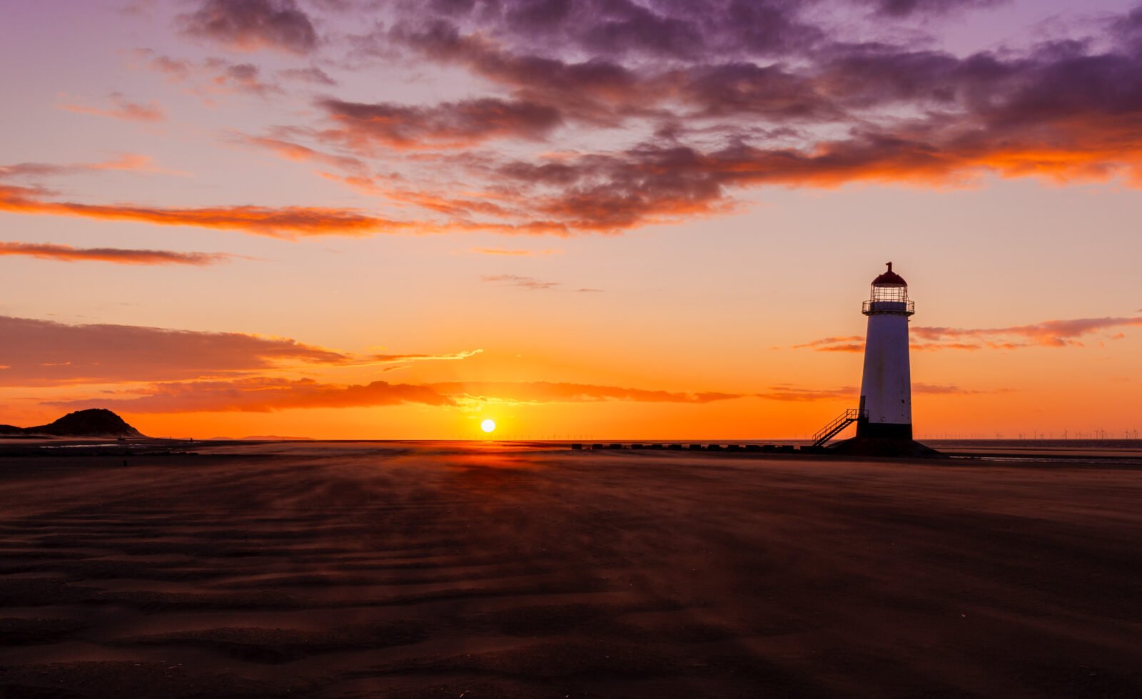 Talacre Lighthouse at sunset on Talacre Beach in North Wales with an orange sky and dramatic clouds